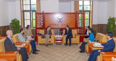 Réunion officielle entre plusieurs personnes assises dans un salon institutionnel lumineux, avec deux interlocuteurs au centre en discussion.